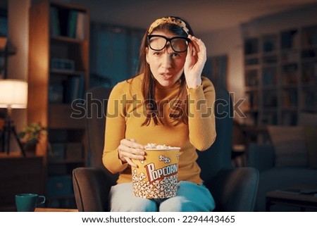 Woman with eye problem watching TV at home, she is lifting her glasses Royalty-Free Stock Photo #2294443465