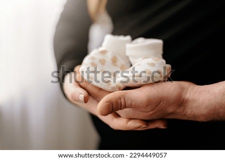 Maternity photo shoot parents holding baby boots on pregnancy belly Royalty-Free Stock Photo #2294449057
