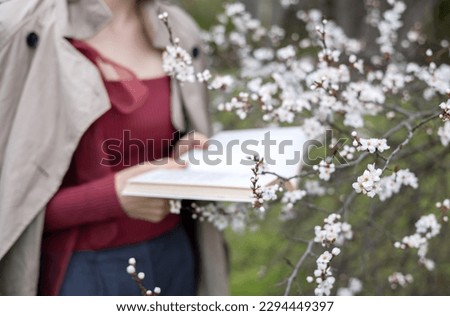 girl in blossom tree flowers holding book in hands.beautiful woman in coat smiling holding branch at eyes.tenderness spring wallpaper.fine delicacy female hugging small white pink flowers,hold in palm