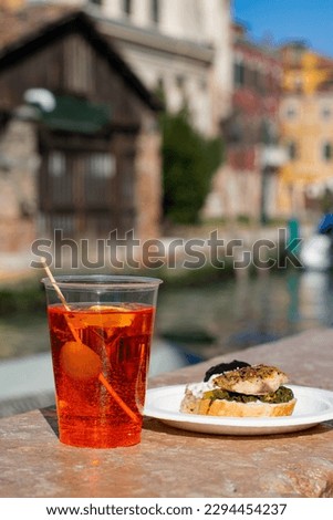 Cocktail Aperol Spritz with olive and Venetian traditional bruschetta Cicchetti on the water canal background in Venice, Italy. Traditional Italian aperitif.