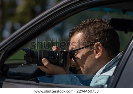 Man in sunglasses with camera sits inside car and takes pictures with professional camera, private detective or paparazzi spy. Journalist seeks sensation and follows celebrities.