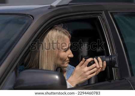 Paparazzi woman or girl sits in her car and takes pictures of famous person. Spy with camera in car. Private detective or paparazzi journalist sitting inside car, taking pictures with camera.