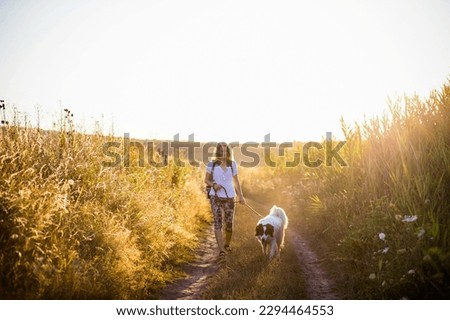 woman walking with dog by the lake at sunset Royalty-Free Stock Photo #2294464553