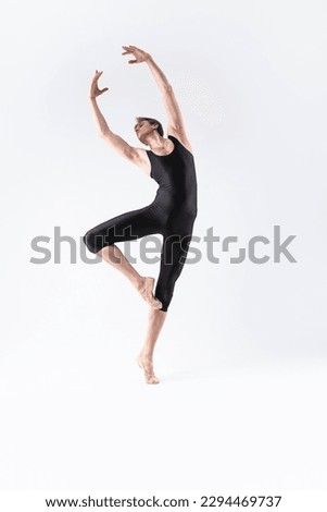 Professional Male Ballet Dancer Young Athletic Man in Black Suit Posing in Ballanced Stretching Dance Pose Studio On White. Vertical image