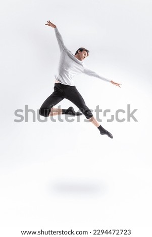 One Caucasian Handsome Young Athlete Man Posing in Flying Ballet Pose with Lifted Hands in White Shirt On White.Vertical Composition