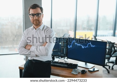 Man trader in formalwear sitting at desk in frot of monitors with charts and data at office