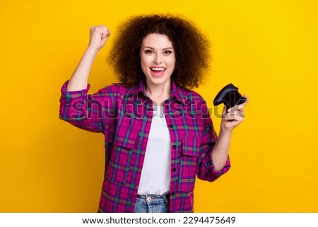 Photo of overjoyed professional young girl cyber player woman raise fist up winner fifa tournament hold gamepad isolated on yellow color background