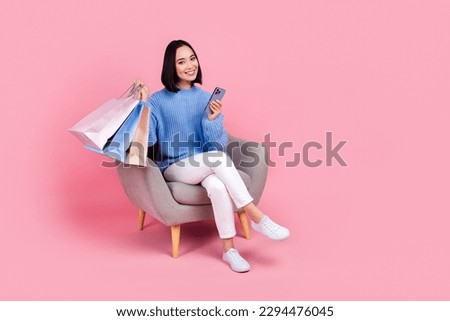 Full length portrait of attractive person sit chair use telephone hold bags isolated on pink color background
