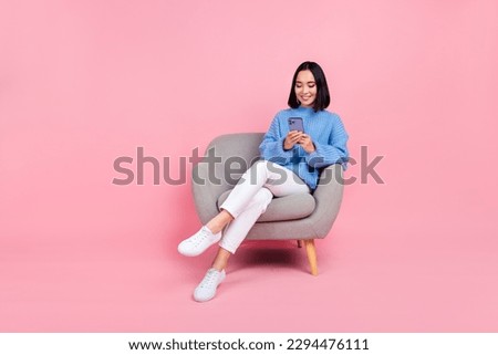 Full length photo of positive nice girl blue sweater white pants sitting on armchair look at smartphone isolated on pink color background Royalty-Free Stock Photo #2294476111