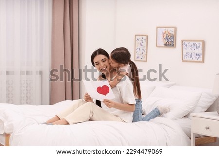 Happy woman with her daughter and handmade greeting card on bed at home. Mother's day celebration