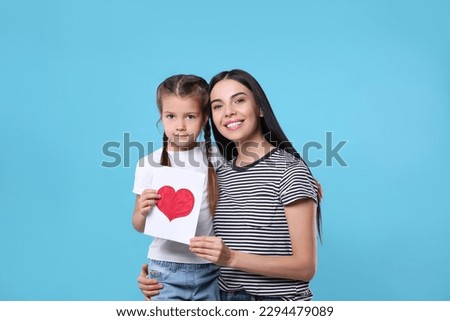 Happy woman with her cute daughter and handmade greeting card on light blue background. Mother's day celebration