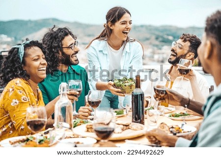 Happy friends dining and drinking red wine glasses on balcony rooftop party - Young people enjoying lunch break at restaurant terrace - Youth lifestyle moments concept with guys and girls hanging out Royalty-Free Stock Photo #2294492629