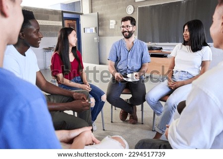 Front view of a diverse group of high school students sitting on chairs in a circle and interacting during a lesson, talking while her classmates and male teacher. High quality photo