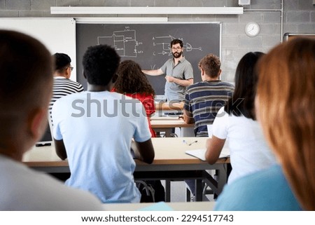 Male Tutor Teaching University Students In Classroom. Rear view from college attending at teacher in class. Professor explains the lesson on the blackboard. High quality photo