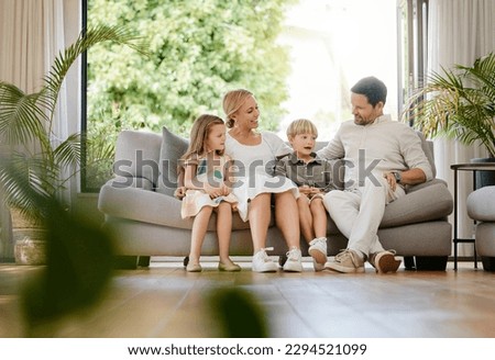 Full body young smiling caucasian family embracing each other and bonding in a home living room on a weekend. Mother and father sitting with children on a sofa. Loving parents and siblings talking Royalty-Free Stock Photo #2294521099