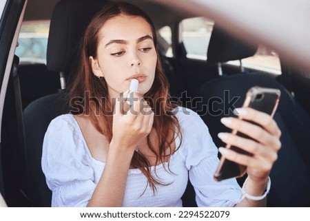 Quickly refreshing her makeup. Shot of a beautiful young woman applying lipstick while sitting in a car.