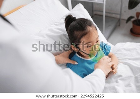 blurred doctor adjusting oxygen mask on sick asian child on hospital bed Royalty-Free Stock Photo #2294522425