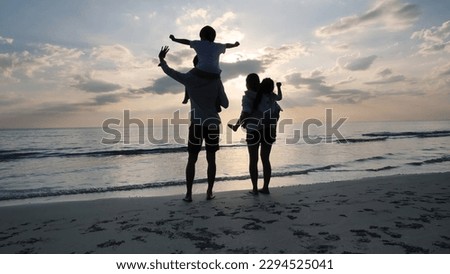 Happy Asian Family On Summer Vacation, a boy on the shoulders of a father, a girl on the back of a mother Looking at the sky on the beach Background sunset in the sea. Travel and Relaxation