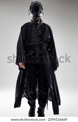 Urbantech outfit cyber style, a young man in stylish black clothes and a mirror mask on the whole face, futuristic style. Studio photo on a light background