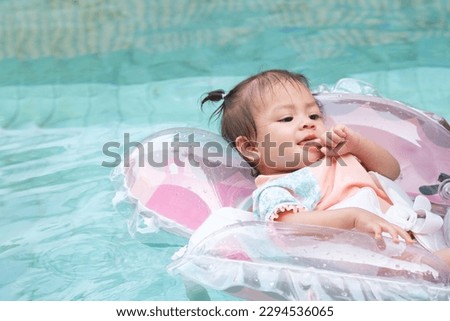 Cute baby girl in swimsuit relaxing on inflatable toy ring floating in pool have fun during summer vacation in tropical resort. Child having fun in swimming pool.