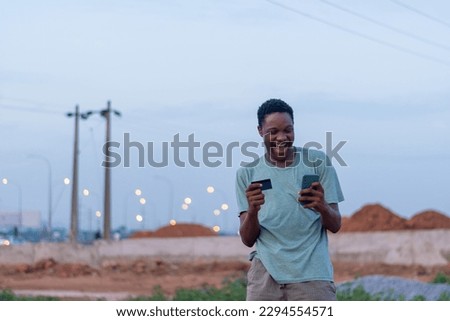 happy african youth using his phone and credit card to make payment online. Buying and shopping concept