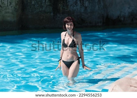 A woman in a bikini enters cold water of the pool. Off season at hotel.
