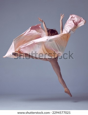 Ballet with silk. One charming professional ballerina wearing silk dress jumping up over grey studio background. Contemporary dance. Concept of classic ballet, inspiration, beauty, motion, creativity