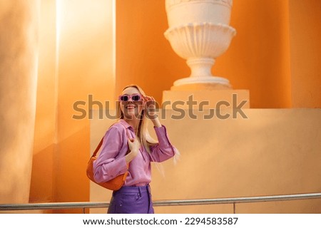 Fashionable happy smiling woman wearing trendy spring, summer outfit with pink sunglasses, satin blouse, purple trousers, orange color faux patent leather baguette bag. Copy, empty space for text Royalty-Free Stock Photo #2294583587