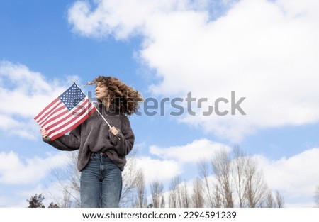adult beautiful young woman 18-20 years old holding american flag in hands against sky. july 4th celebration. Independence Day of the United States of America. Pride, freedom, national identity Royalty-Free Stock Photo #2294591239