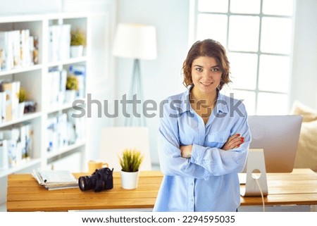 Smiling female photographer with a professional camera standing near desk.