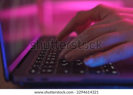 Person typing at laptop computer at night. Female uses keyboard, shakes buttons with fingers. Internet security, cyber attack. Trendy neon light. Creative vivid color of ultraviolet red and blue. Royalty-Free Stock Photo #2294614321
