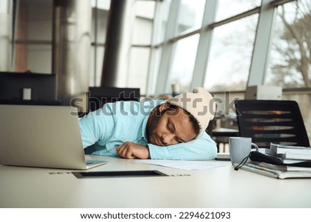 Man in hat relaxing on desk in the office Royalty-Free Stock Photo #2294621093