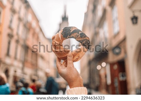 Beautiful young female tourist in stylish clothes holding pretzel obwarzanek on the market square in Krakow in Poland. High quality photo Royalty-Free Stock Photo #2294636323