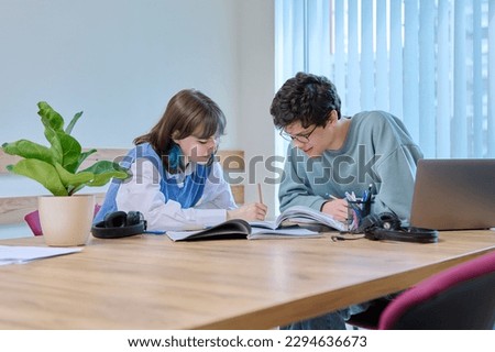 College students teenage guy girl talking sitting together at desk in classroom Royalty-Free Stock Photo #2294636673