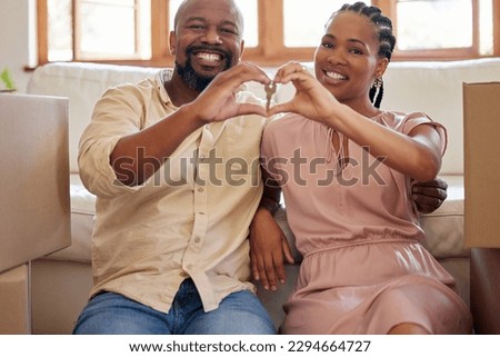 A couple holding keys, making a heart sign with their hands at home. Portrait of a smiling, happy african american man and woman in love, sitting in the lounge of their new home, looking at the camera Royalty-Free Stock Photo #2294664727