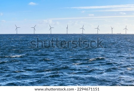 Sea with a row of offshore wind turbines in distance on a sunny day. Royalty-Free Stock Photo #2294671151