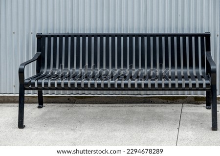 Black Metal Bench on White Concrete with a  Silver Corrugated Wall Backdrop. 