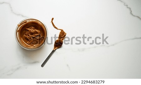 Salted Caramel sauce in glass bowl on white marble background. Next to it lies a spoon soiled in caramel. Butter, sugar with cream and salt. Top view food photo.