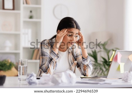 A tired young Indian girl gets angry from the number of tasks, crumples up the paper and throws it away, tries to calm down by meditating. Stressful work and study, overtasking, headache. Royalty-Free Stock Photo #2294696539