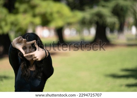 A beautiful teenage girl looks through a frame made up of hands. Attractive teenage girl make frame by fingers, isolated on blur background with copy space for text.