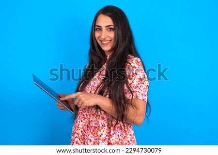 Photo of happy cheerful smart beautiful brunette woman wearing floral dress over blue background hold tablet browsing internet