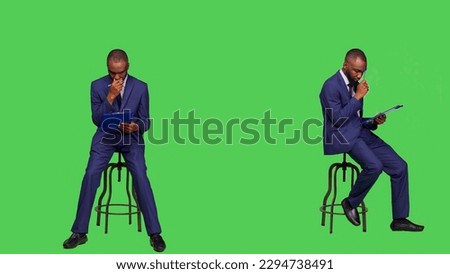 African american man thinking about business notes on papers, brainstorming new ideas on clipboard files. Young business person sitting on chair in studio, feeling thoughtful and pensive.