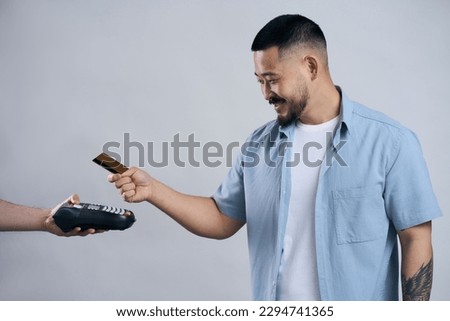 Attractive smiling asian man holding credit card making payment using credit card machine, isolated on gray background . Shopping, wireless technology concept                             