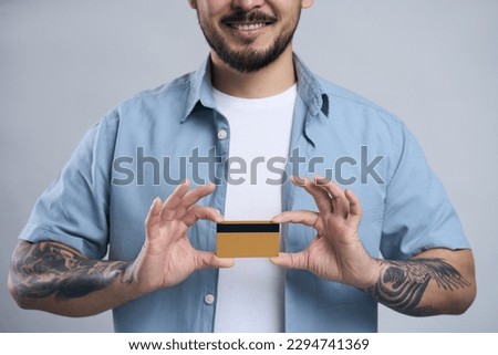 Young smiling Korean man holding credit card, showing ok sign looking at camera isolated on gray background. Shopping, electronic money concept