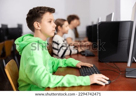 Smart focused tween boy studying with classmates in modern computer lab at school.. Royalty-Free Stock Photo #2294742471