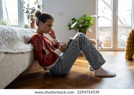 Teens and cyberbullying. Upset teen girl sitting on floor near bed using smartphone at home, scrolling social media. Child spending too much time on phone. Teenagers and gadget addiction Royalty-Free Stock Photo #2294754539