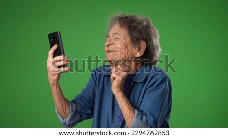 Funny crazy happy elderly old toothless woman taking selfie using mobile cell phone isolated on solid green screen background studio portrait.