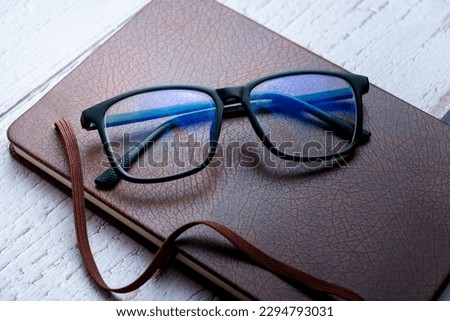 black frame blue light blocking technology anti glare spectacles glasses on brown textured book wooden background Royalty-Free Stock Photo #2294793031