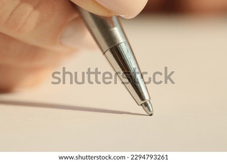 Hand of woman holding iron ball-pen ready to write on blank paper sheet in notepad. Female employee makes notes of project details at work