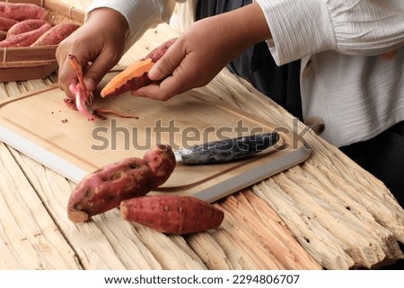 Peeled Red Sweet Potato, Female Hand Hold Peeler Knife on Wooden Table 